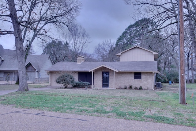 view of front of property featuring central air condition unit, brick siding, and a front yard