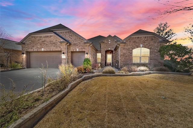 french country inspired facade with a front yard, brick siding, a garage, and driveway