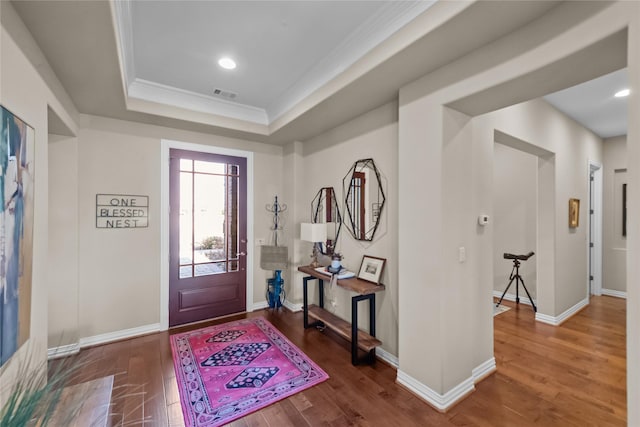 entryway featuring a tray ceiling, wood finished floors, visible vents, and baseboards