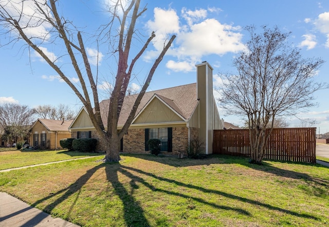 view of front of home featuring fence, a front yard, a shingled roof, brick siding, and a chimney