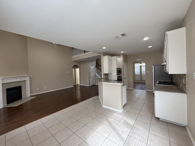 kitchen with visible vents, open floor plan, a fireplace with flush hearth, light tile patterned floors, and arched walkways