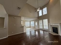 unfurnished living room featuring wood finished floors, a high ceiling, a fireplace, and visible vents