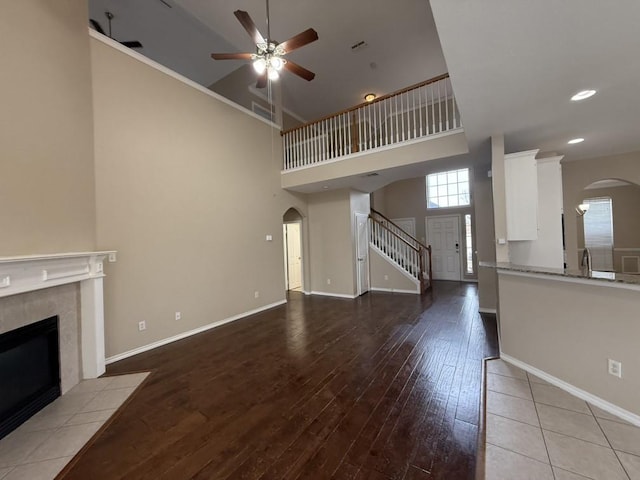 unfurnished living room with arched walkways, a tiled fireplace, baseboards, and wood finished floors