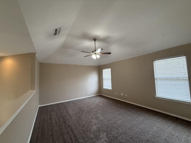 empty room with visible vents, ceiling fan, baseboards, dark carpet, and vaulted ceiling