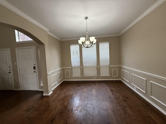 unfurnished dining area featuring ornamental molding, dark wood-style floors, arched walkways, a decorative wall, and a chandelier