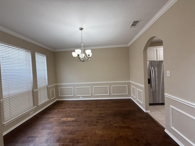 unfurnished dining area featuring visible vents, ornamental molding, wood finished floors, arched walkways, and a notable chandelier