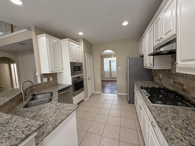 kitchen with arched walkways, stainless steel appliances, a sink, white cabinets, and under cabinet range hood