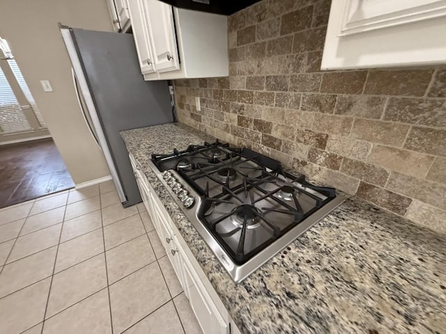 kitchen with tasteful backsplash, appliances with stainless steel finishes, white cabinets, light tile patterned floors, and light stone countertops