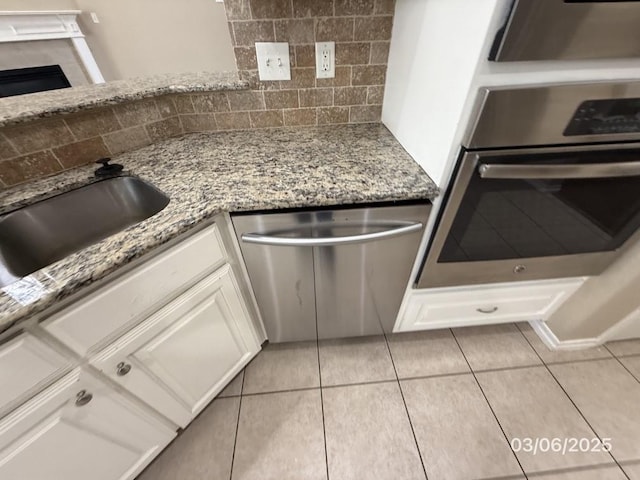 kitchen featuring white cabinets, backsplash, light stone countertops, and appliances with stainless steel finishes