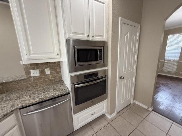 kitchen featuring tasteful backsplash, white cabinetry, arched walkways, appliances with stainless steel finishes, and light tile patterned flooring