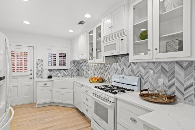 kitchen with visible vents, light stone counters, white cabinets, white appliances, and a sink