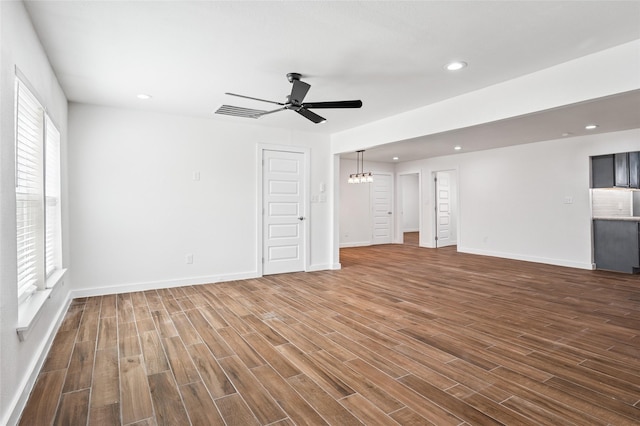 unfurnished living room featuring recessed lighting, ceiling fan with notable chandelier, baseboards, and dark wood-style flooring