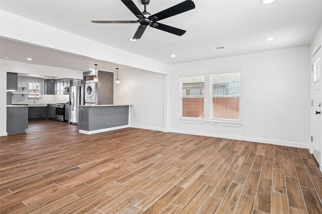 unfurnished living room with stacked washer / dryer, plenty of natural light, wood finished floors, and visible vents