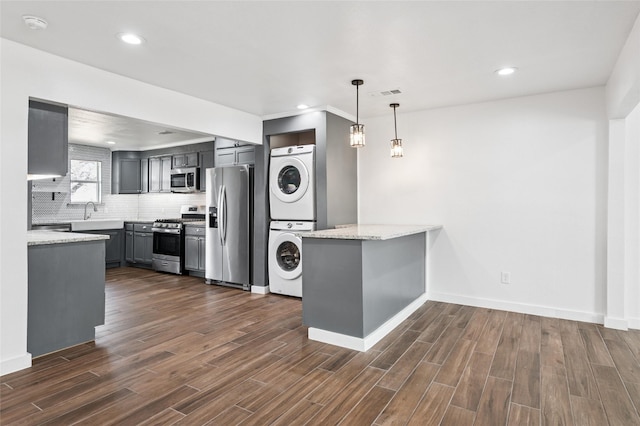 kitchen featuring stainless steel appliances, tasteful backsplash, dark wood-type flooring, and stacked washer and clothes dryer