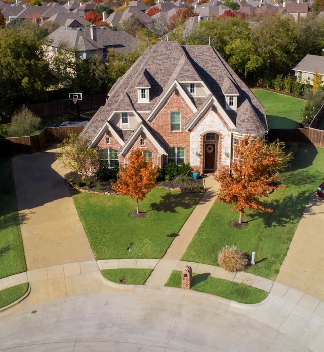 view of front of house featuring stone siding, a shingled roof, a front lawn, and fence