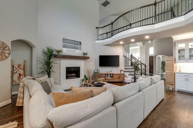 living room with stairway, visible vents, a fireplace, arched walkways, and dark wood-type flooring