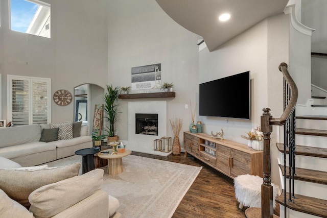 living room with stairway, a fireplace, arched walkways, dark wood-type flooring, and a towering ceiling