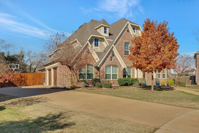 tudor home featuring fence, driveway, a shingled roof, a front lawn, and brick siding