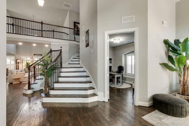 stairway with a high ceiling, wood finished floors, and visible vents