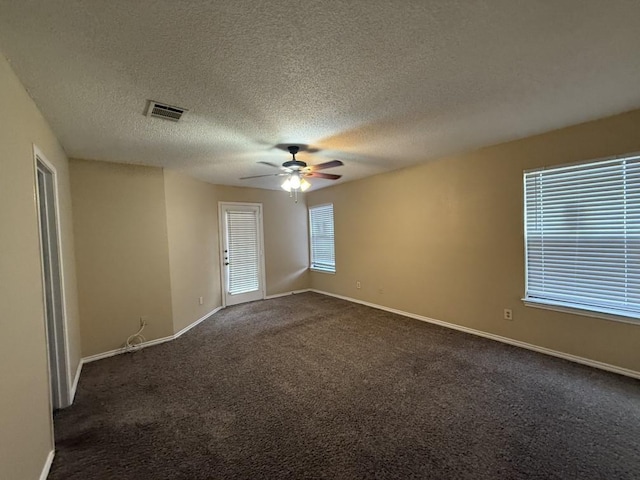 unfurnished room with visible vents, a textured ceiling, dark colored carpet, baseboards, and ceiling fan