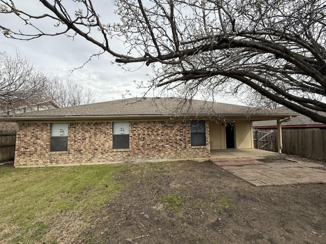 back of property with brick siding, roof with shingles, a yard, and fence