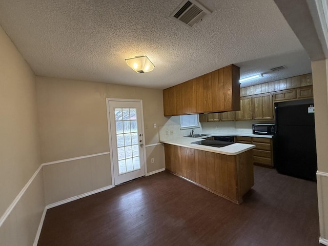 kitchen featuring visible vents, brown cabinets, black appliances, a peninsula, and light countertops