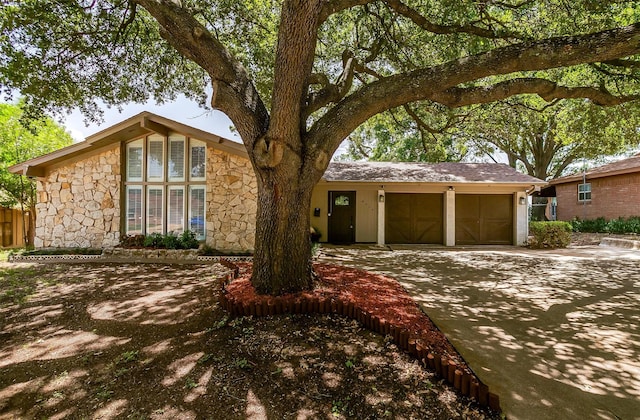 mid-century modern home featuring a garage, stone siding, and driveway