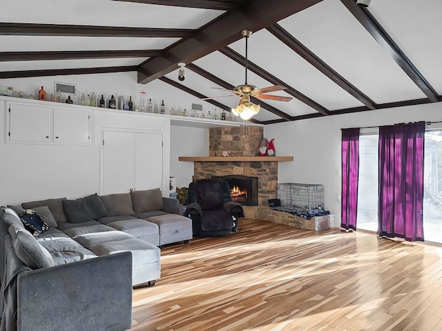 living room featuring visible vents, a ceiling fan, a stone fireplace, light wood finished floors, and vaulted ceiling with beams