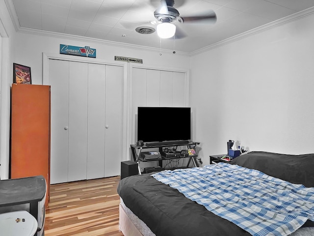 bedroom featuring crown molding, light wood-style floors, visible vents, and ceiling fan