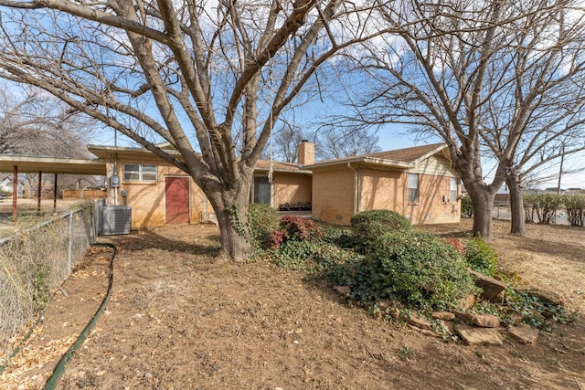 exterior space featuring brick siding, central AC unit, a chimney, and fence