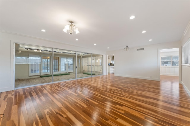 unfurnished living room with wood finished floors, visible vents, baseboards, recessed lighting, and a notable chandelier