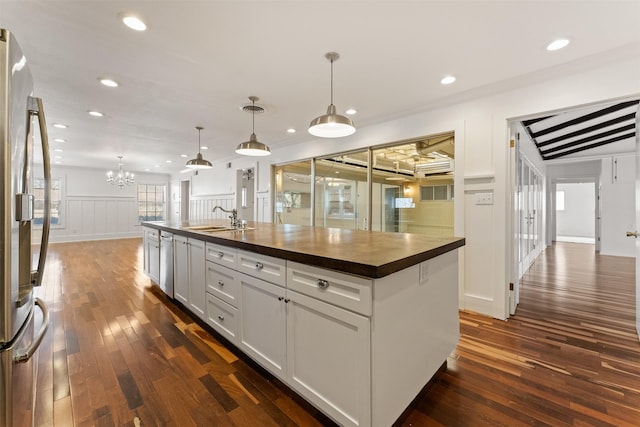 kitchen featuring dark wood-style floors, wooden counters, a kitchen island with sink, a sink, and appliances with stainless steel finishes