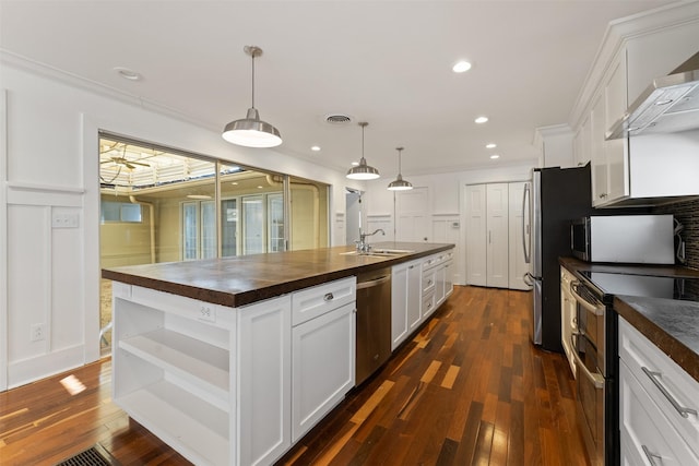 kitchen featuring a center island with sink, wooden counters, a sink, stainless steel appliances, and white cabinetry