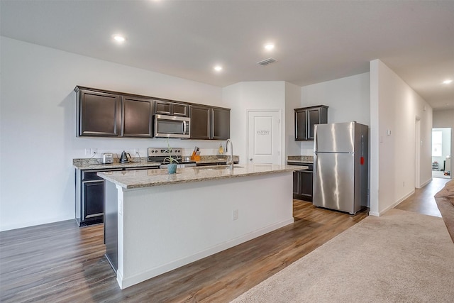 kitchen featuring visible vents, an island with sink, a sink, dark brown cabinets, and appliances with stainless steel finishes