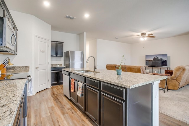 kitchen featuring light wood-type flooring, a kitchen island with sink, a sink, open floor plan, and stainless steel appliances