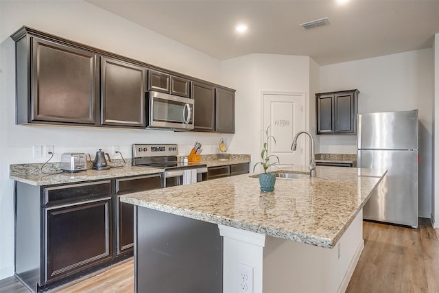 kitchen with visible vents, light wood-style flooring, a sink, stainless steel appliances, and light stone countertops