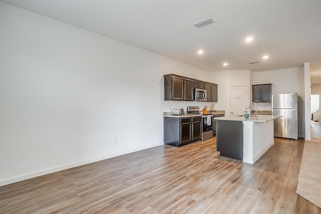 kitchen with visible vents, an island with sink, light wood-style floors, appliances with stainless steel finishes, and dark brown cabinets