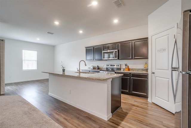 kitchen featuring visible vents, a sink, light wood-style flooring, appliances with stainless steel finishes, and a kitchen island with sink