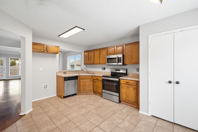 kitchen with light countertops, appliances with stainless steel finishes, brown cabinetry, a textured ceiling, and a sink