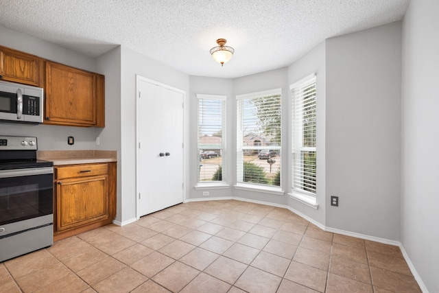 kitchen featuring light tile patterned floors, appliances with stainless steel finishes, brown cabinetry, and light countertops