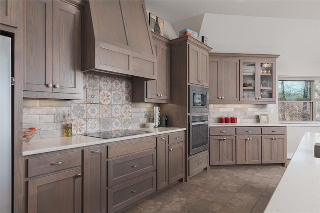 kitchen featuring tasteful backsplash, appliances with stainless steel finishes, light countertops, glass insert cabinets, and custom exhaust hood