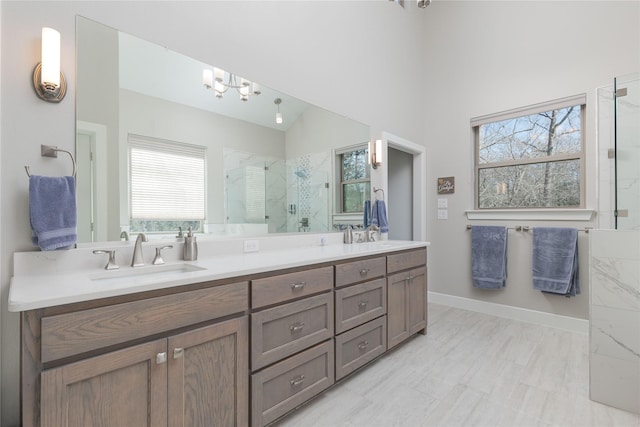 full bathroom featuring a shower with door, double vanity, baseboards, and a sink