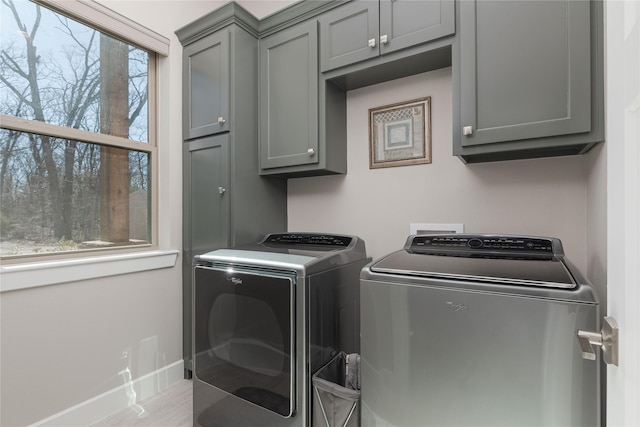 clothes washing area with washer and dryer, cabinet space, and baseboards