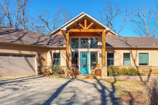 view of front of house featuring an attached garage, stone siding, and roof with shingles