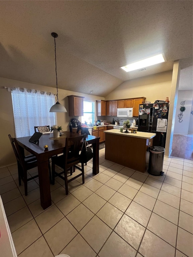 kitchen with a kitchen island, black fridge with ice dispenser, light tile patterned flooring, light countertops, and white microwave