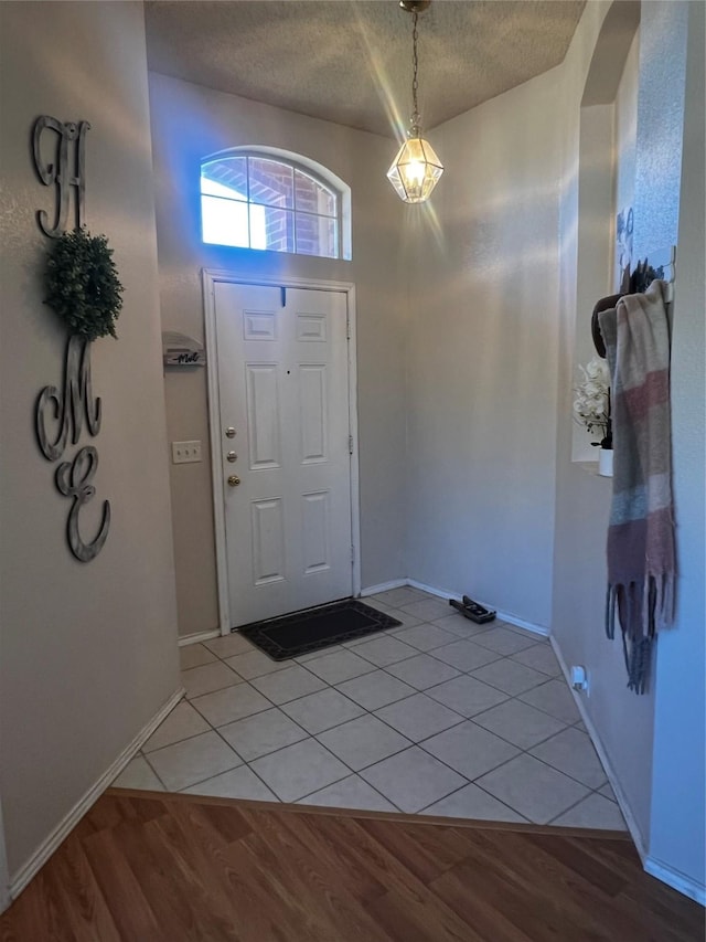 foyer with light tile patterned floors, baseboards, a textured ceiling, and arched walkways