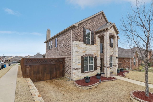 view of front of property featuring brick siding, stone siding, driveway, and fence