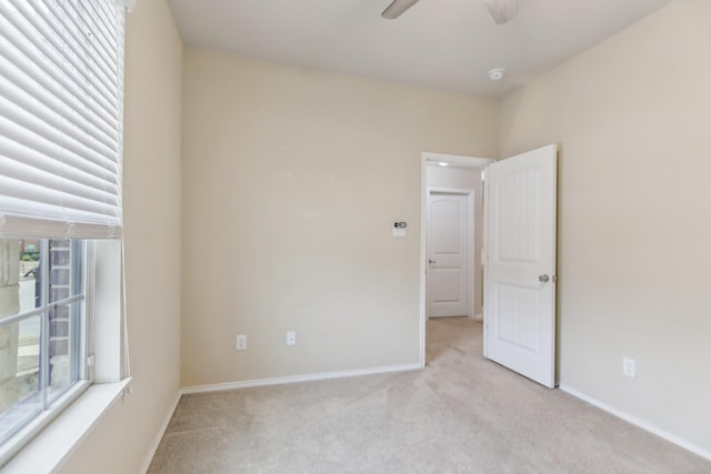 unfurnished room with light colored carpet, a ceiling fan, and baseboards