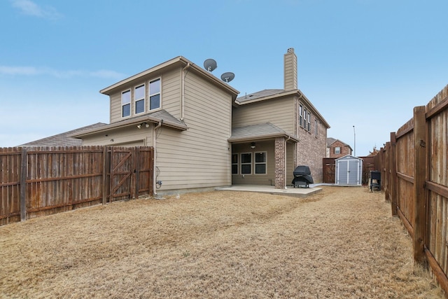 rear view of property featuring brick siding, a fenced backyard, an outbuilding, a storage unit, and a patio