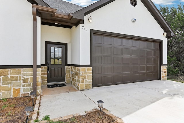 doorway to property featuring concrete driveway, stone siding, roof with shingles, and stucco siding